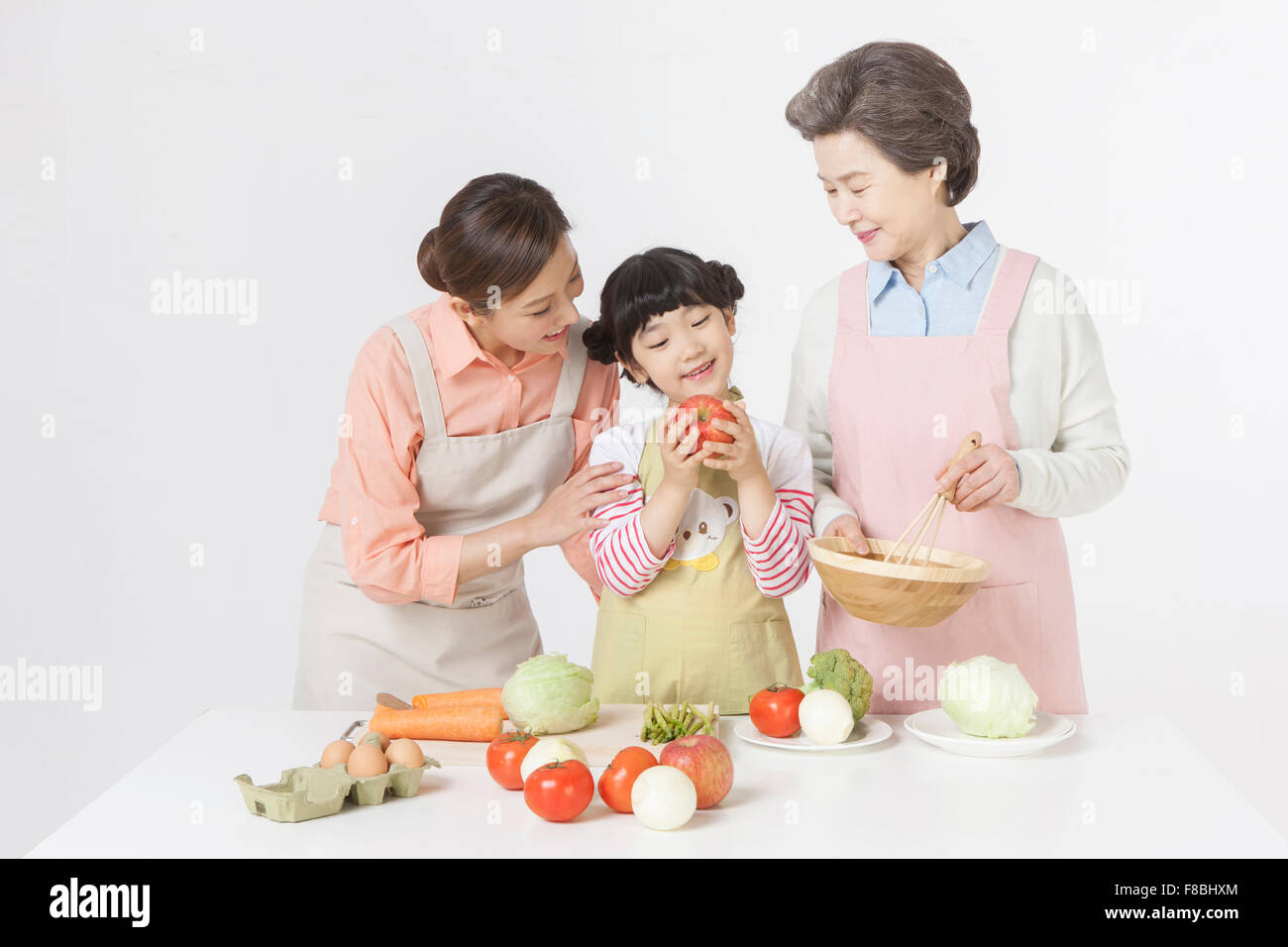 Mother, daughter, and grandmother in apron cooking together Stock Photo