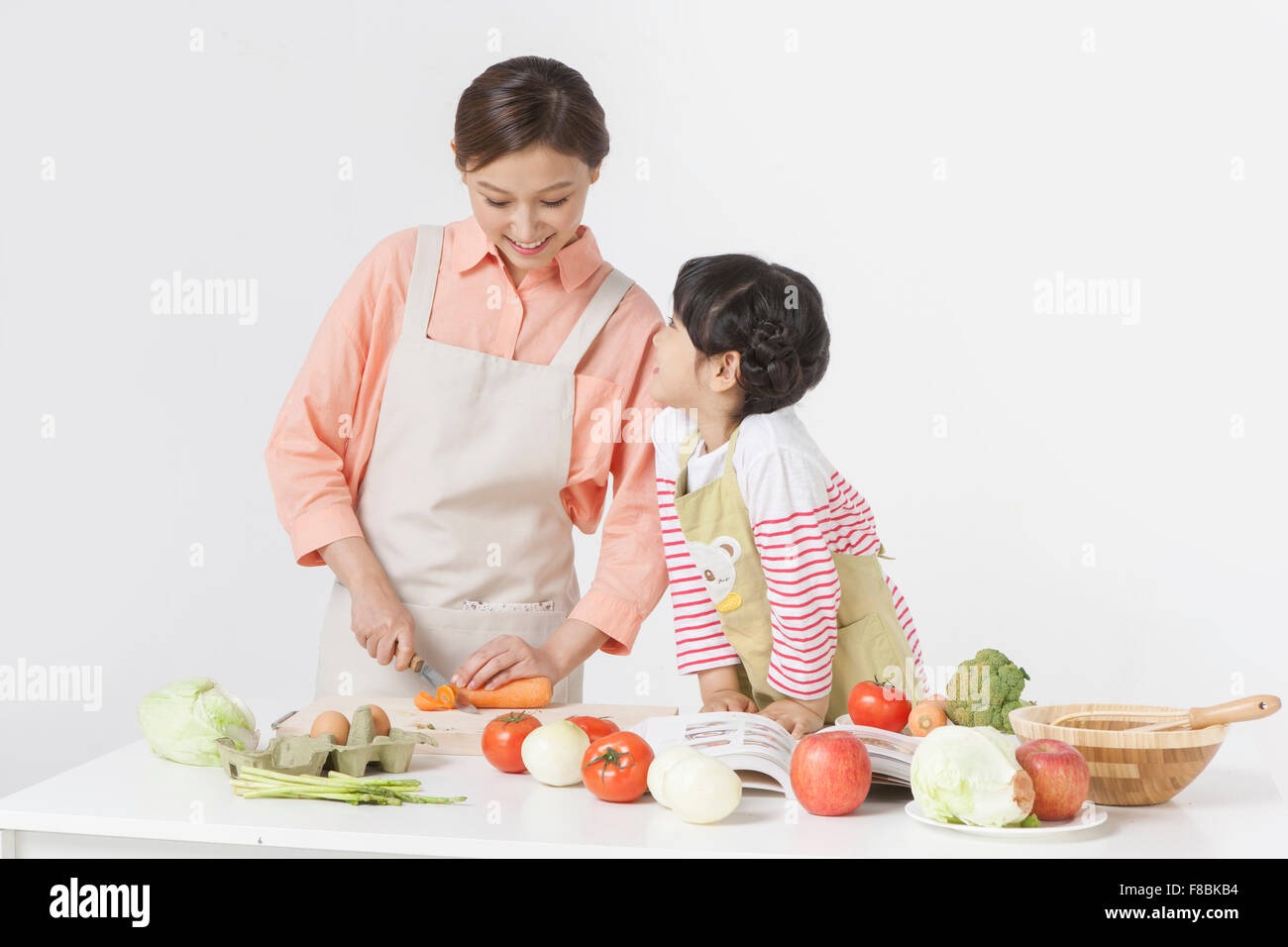 Mother chopping a carrot and her daughter looking at her mom both in