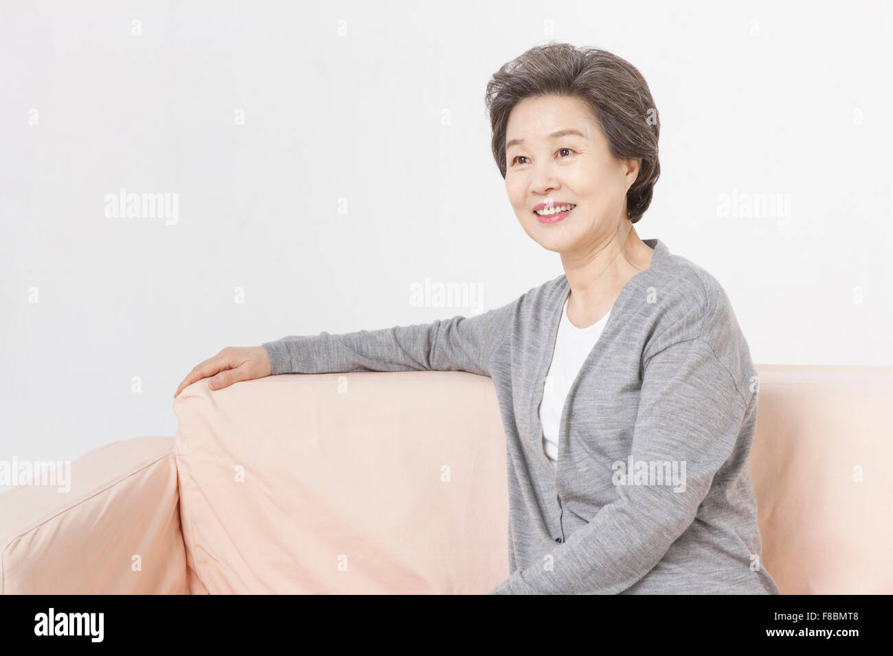 Senior woman sitting on a couch with her arm rested on the back Stock
