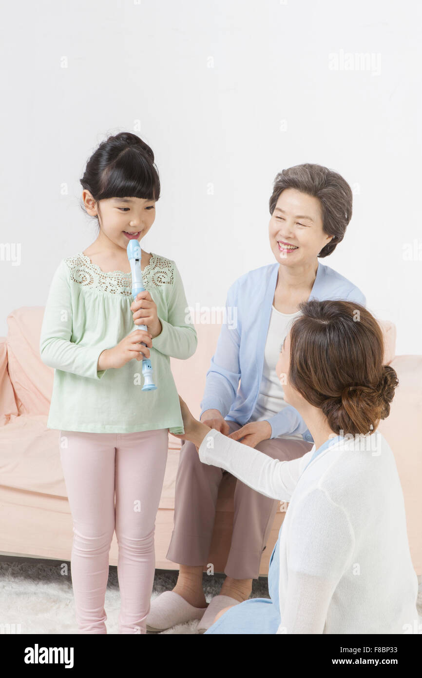 Granddaughter playing musical instrument and her mother and grandmother looking at her being happy Stock Photo