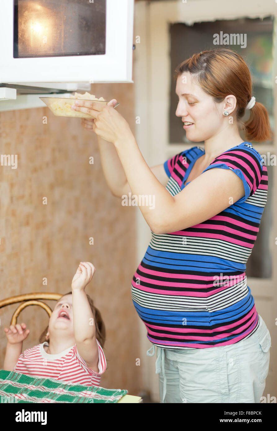 pregnant woman with child cooks with  microwave oven Stock Photo
