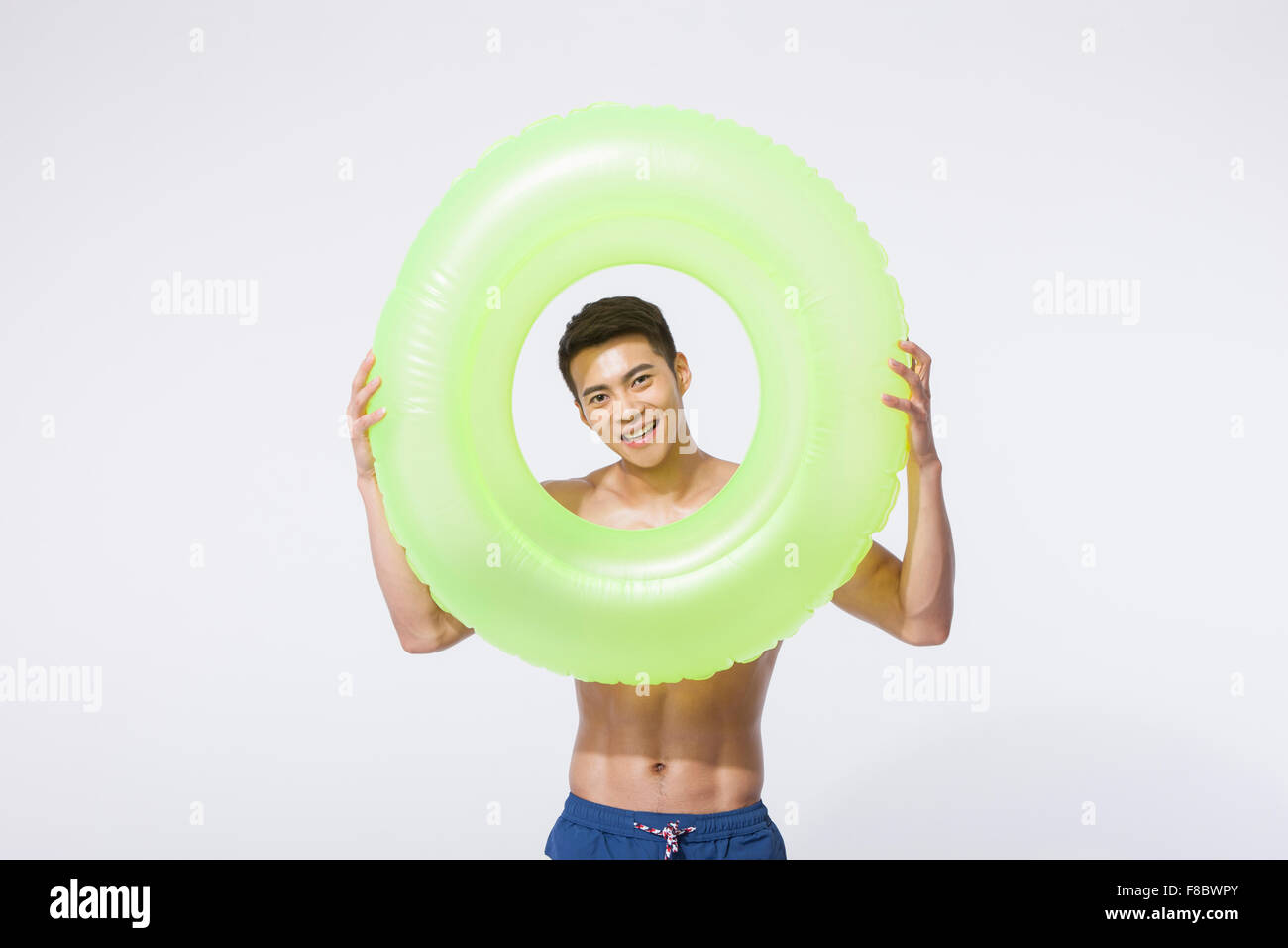 Muscular man in swimming pants holding a ring tube and looking through it Stock Photo