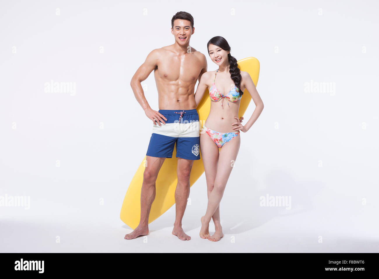 Muscular man and woman in swimming wear standing with a surfing board both staring forward with a smile Stock Photo