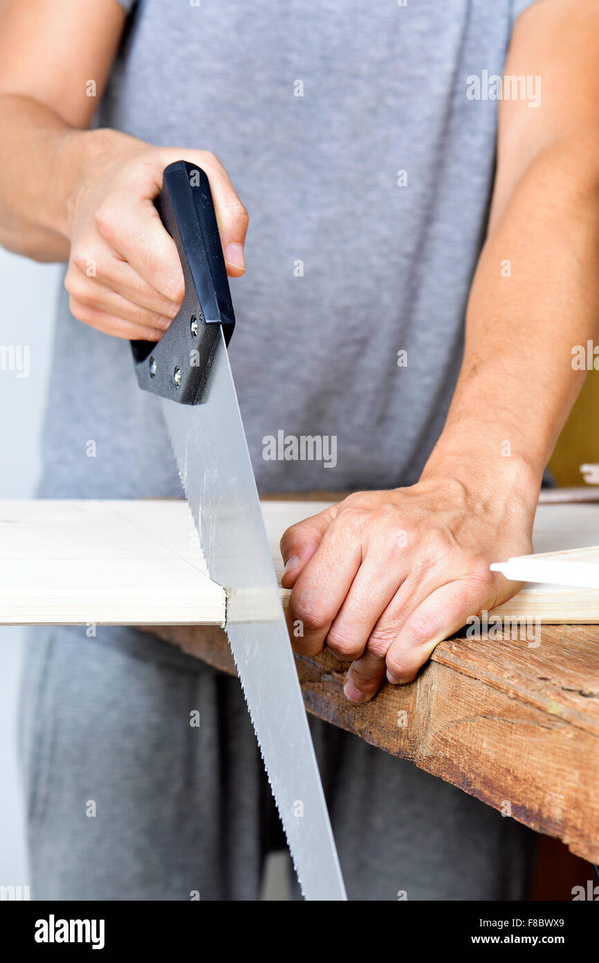 closeup of a young caucasian man sawing a wooden board with a handsaw Stock Photo