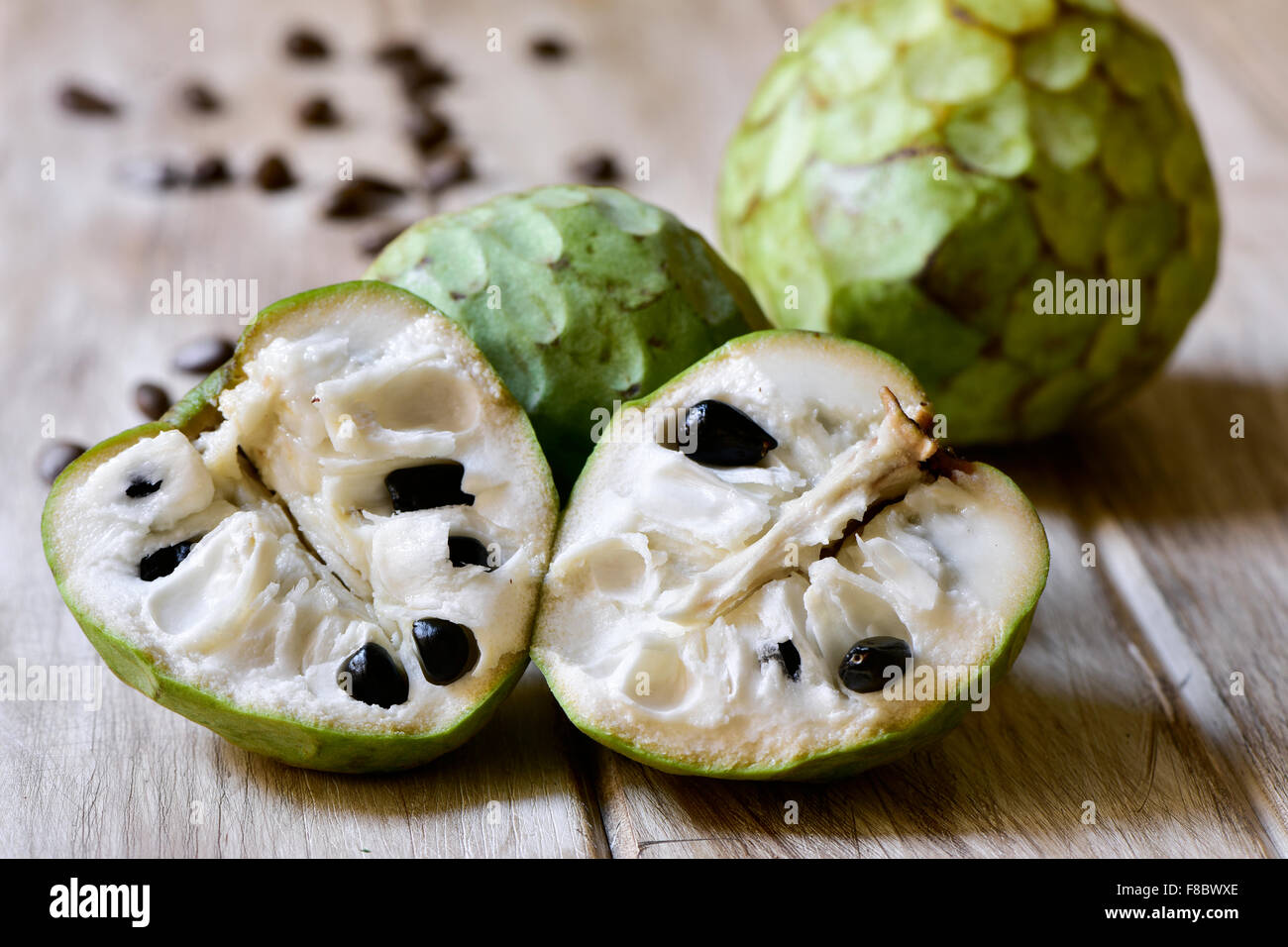 closeup of some custard apples, one of them cut in half, on a rustic wooden surface Stock Photo