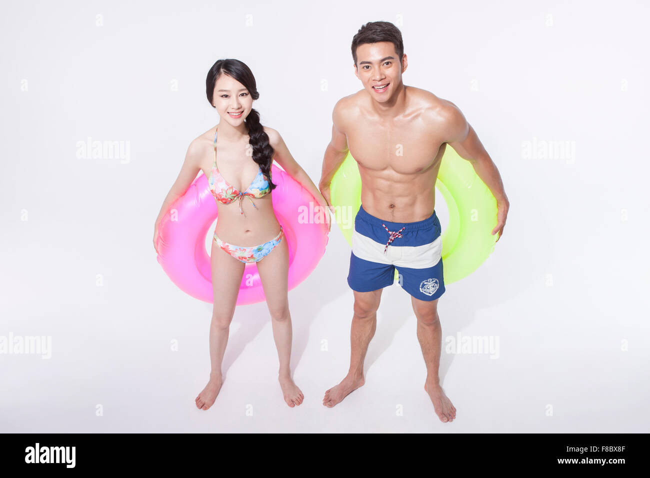 High angle of a couple in swimming wear holding a ring tube behind their back both staring upward and smiling Stock Photo