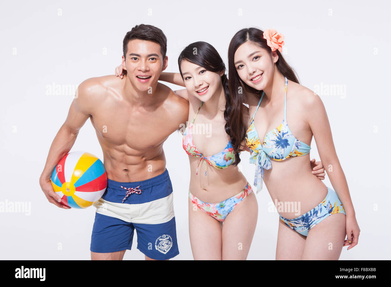 Two women in bikini and a man in swimming pants holding a beach ball  putting their arms around each other's shoulder and smiling Stock Photo -  Alamy
