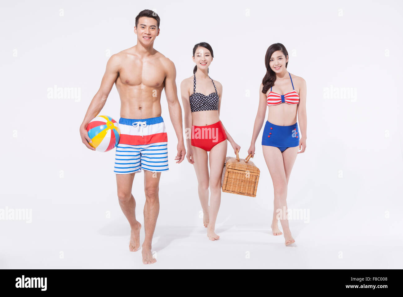 Two women in retro style bikini and a man in swimming pants holding a beach  ball and picnic box and walking together Stock Photo - Alamy