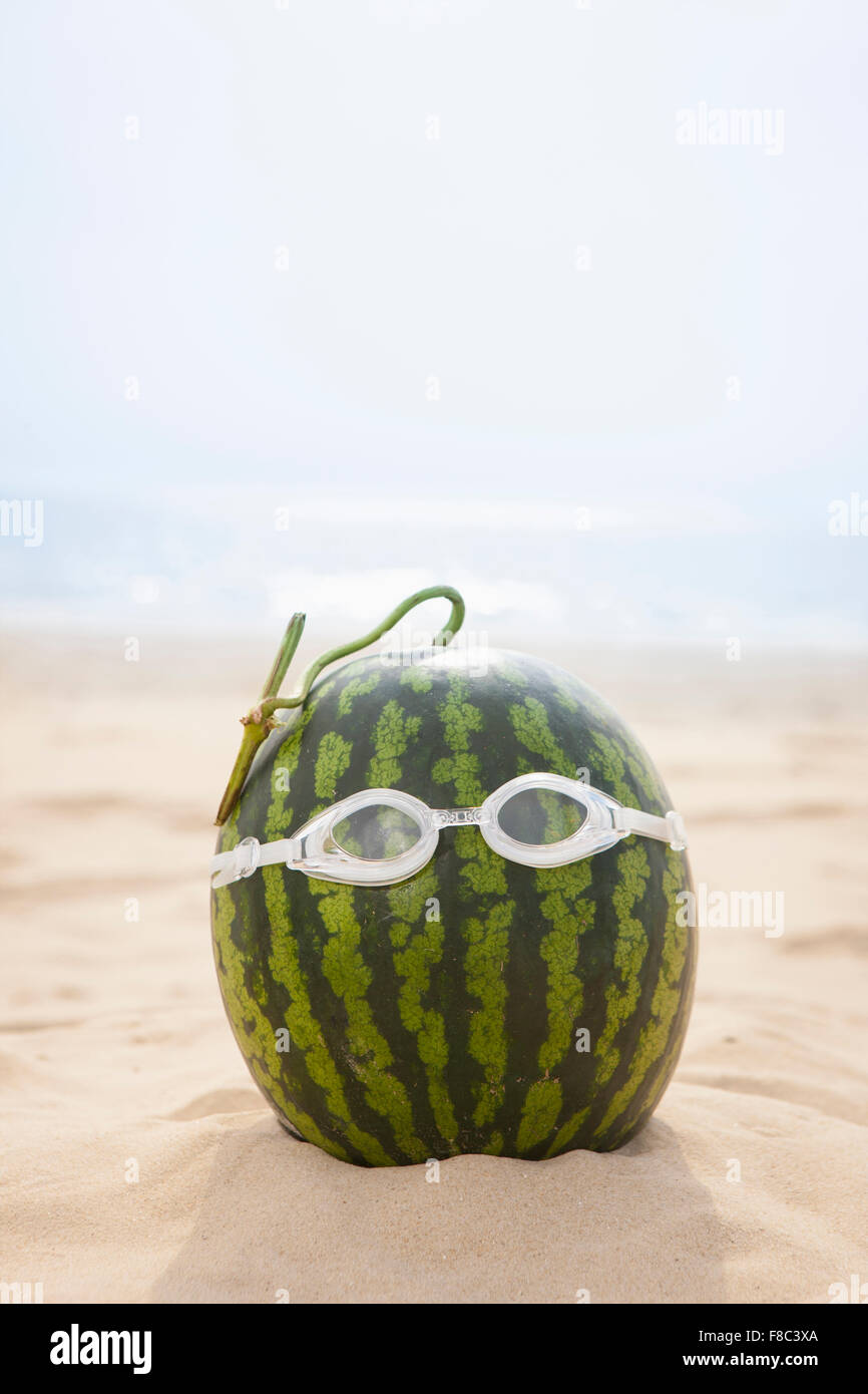 Watermelon wearing swimming goggles placed on sand out of focus Stock Photo