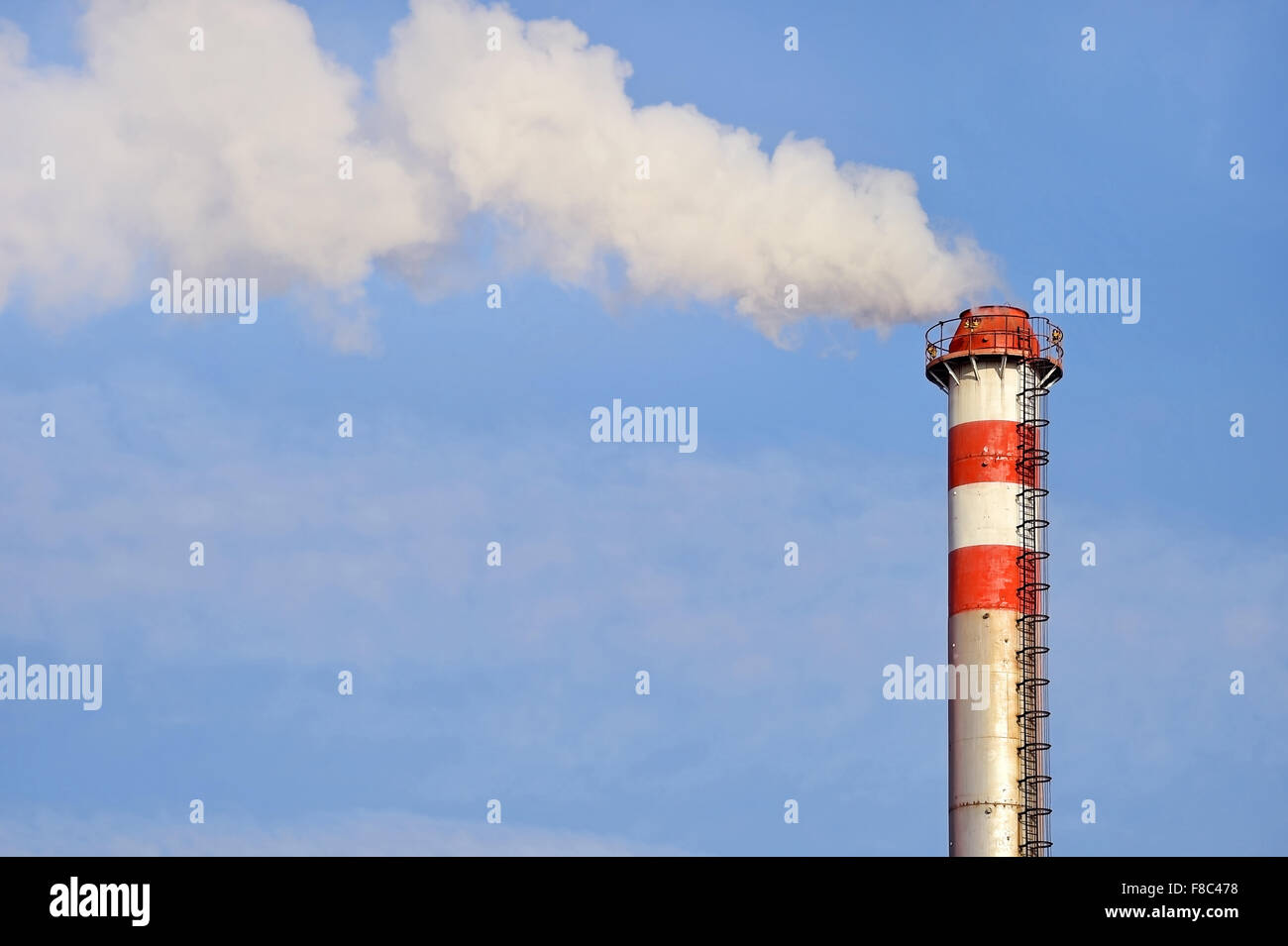 Smoke and steam coming out from a industrial petrochemical plant chimney with a blue sky on the background Stock Photo