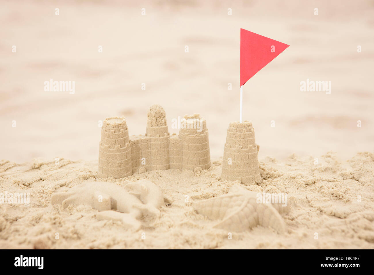 Sandcastle with red flag on sand out of focus Stock Photo - Alamy