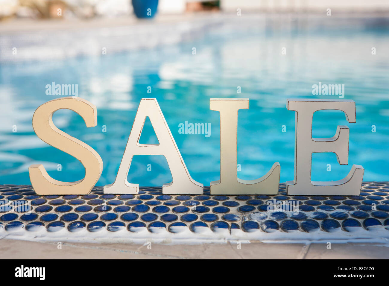 English characters of SALE standing on blue tiles at the edge of the swimming pool Stock Photo