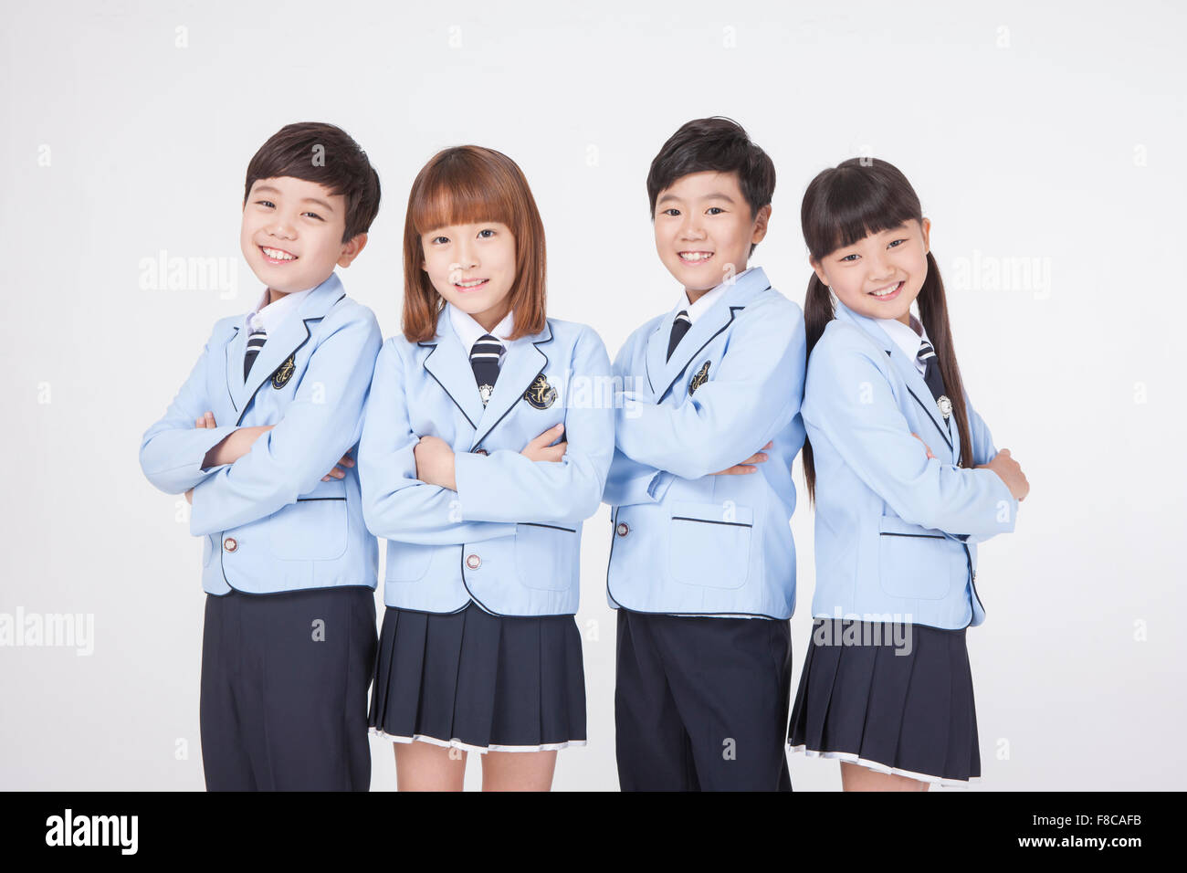Four elementary school age kids in school uniforms consisting of two girls and two boys standing together with their arms folded Stock Photo
