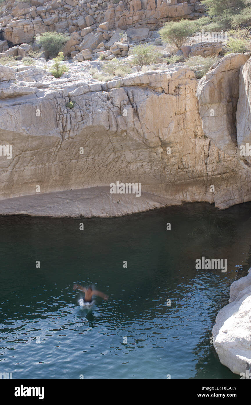 Man jumps from a cliff at Wadi Bani Khalid, a natural canyon formation of rocks and crystal clear pools Stock Photo