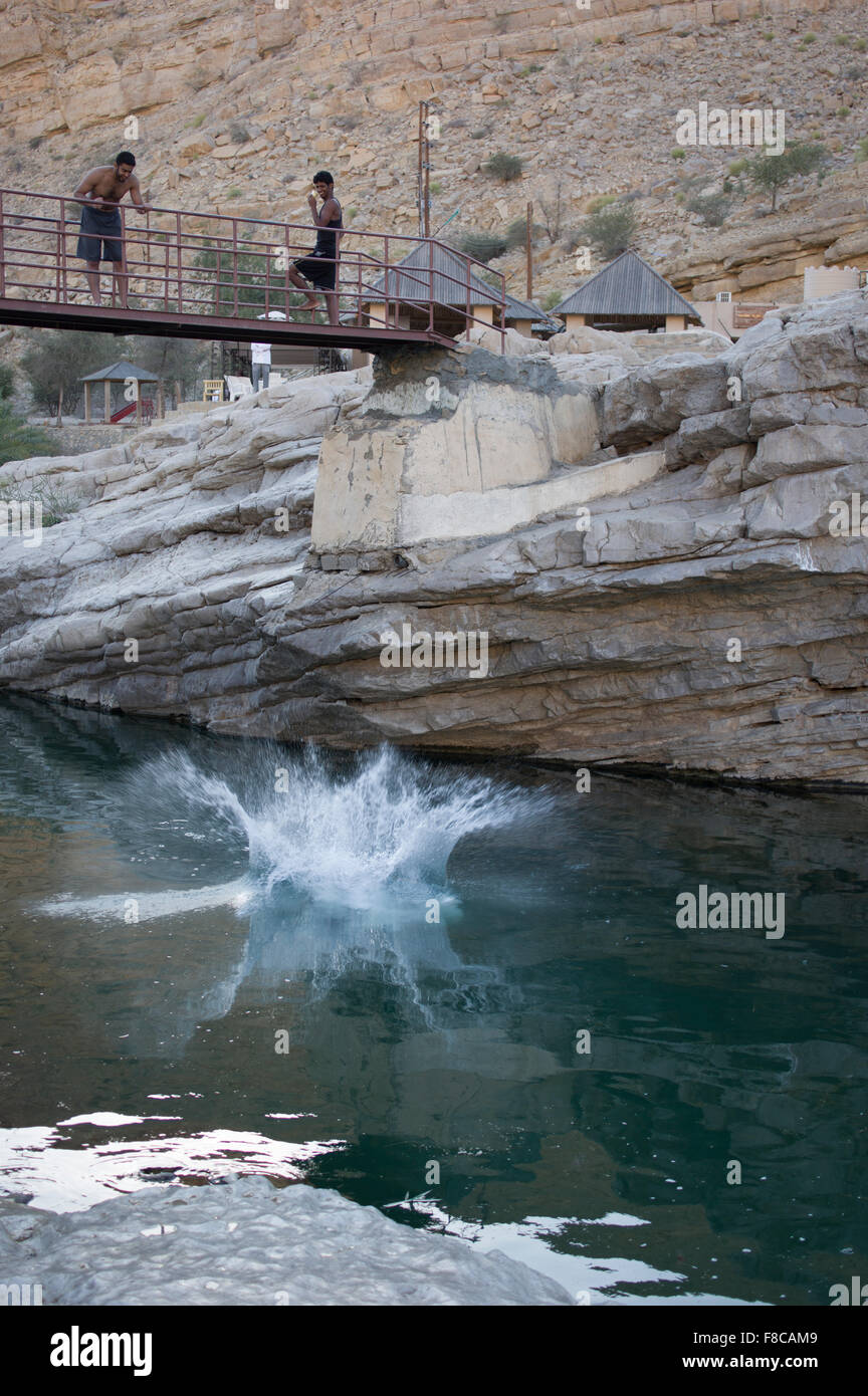 Man belly flops from a bridge into the water at Wadi Bani Khalid, a natural canyon formation of rocks and crystal clear pools Stock Photo