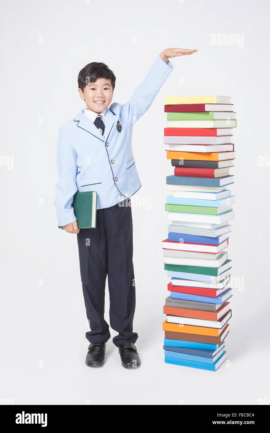 Elementary school age boy in school uniforms holding a book and standing next to a pile of books with a hand gesture meaning Stock Photo