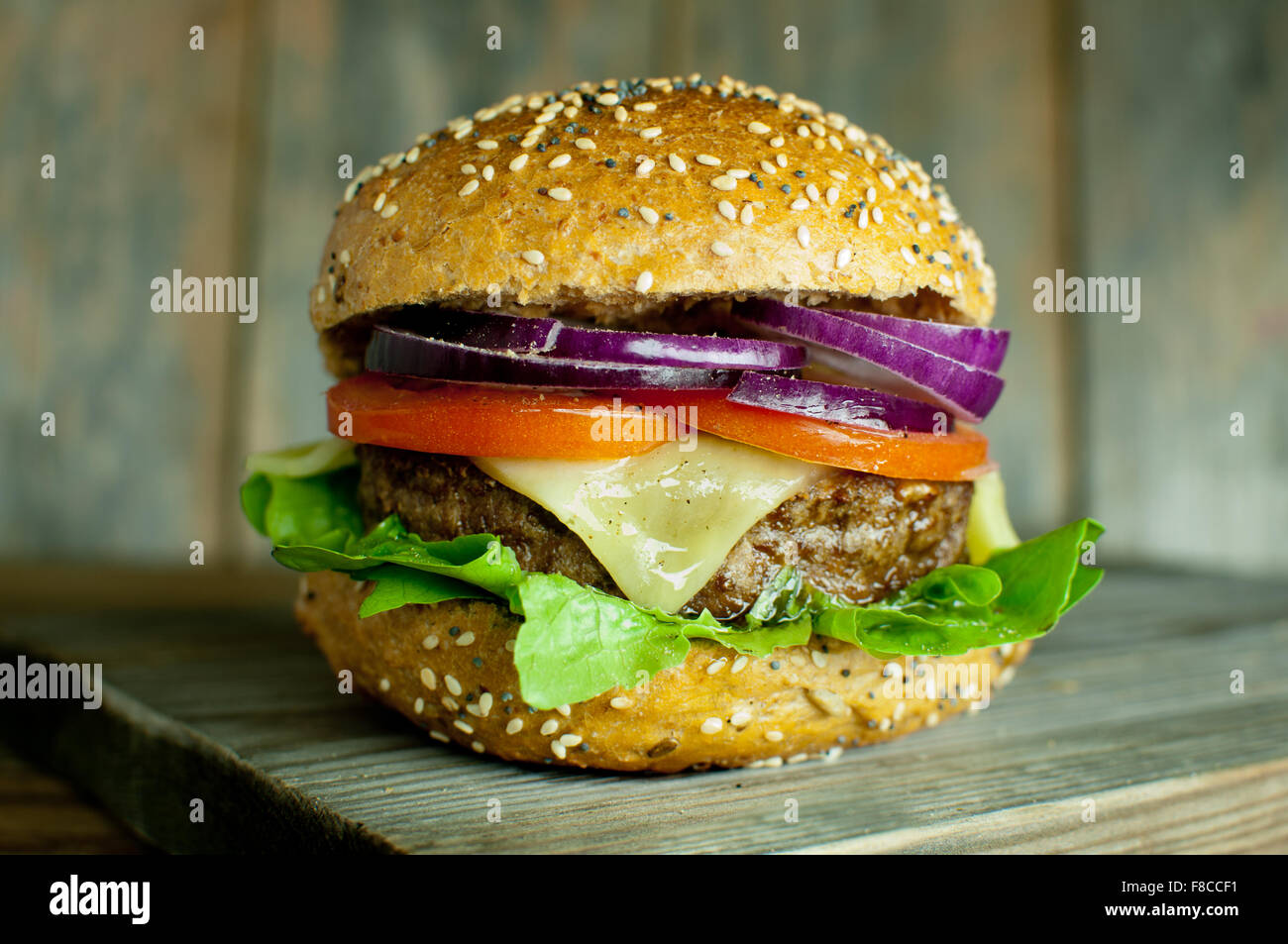 Cheese burger with tomato and onion filling on top of a wooden chopping board Stock Photo