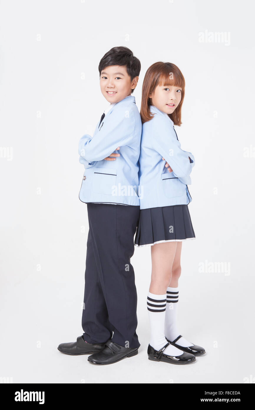 Elementary school boy and girl in school uniforms standing back to back each other with their arms folded and staring forward Stock Photo