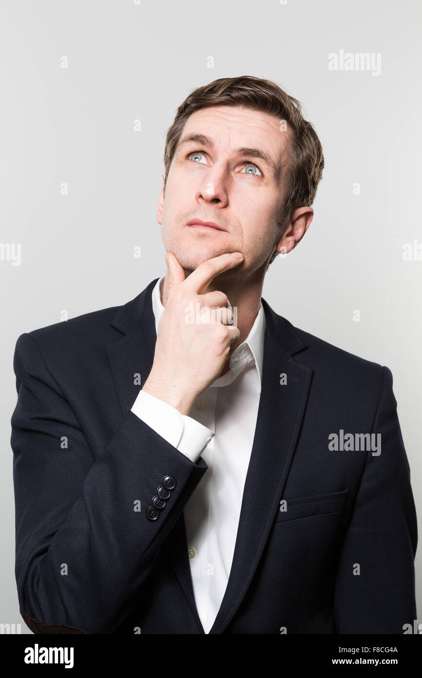 Blond-haired european businessman with a thoughtful look stares to the ceiling while in front of a gradient background Stock Photo