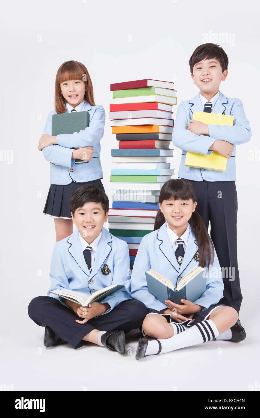 Four elementary school students holding a book and standing and sitting ...