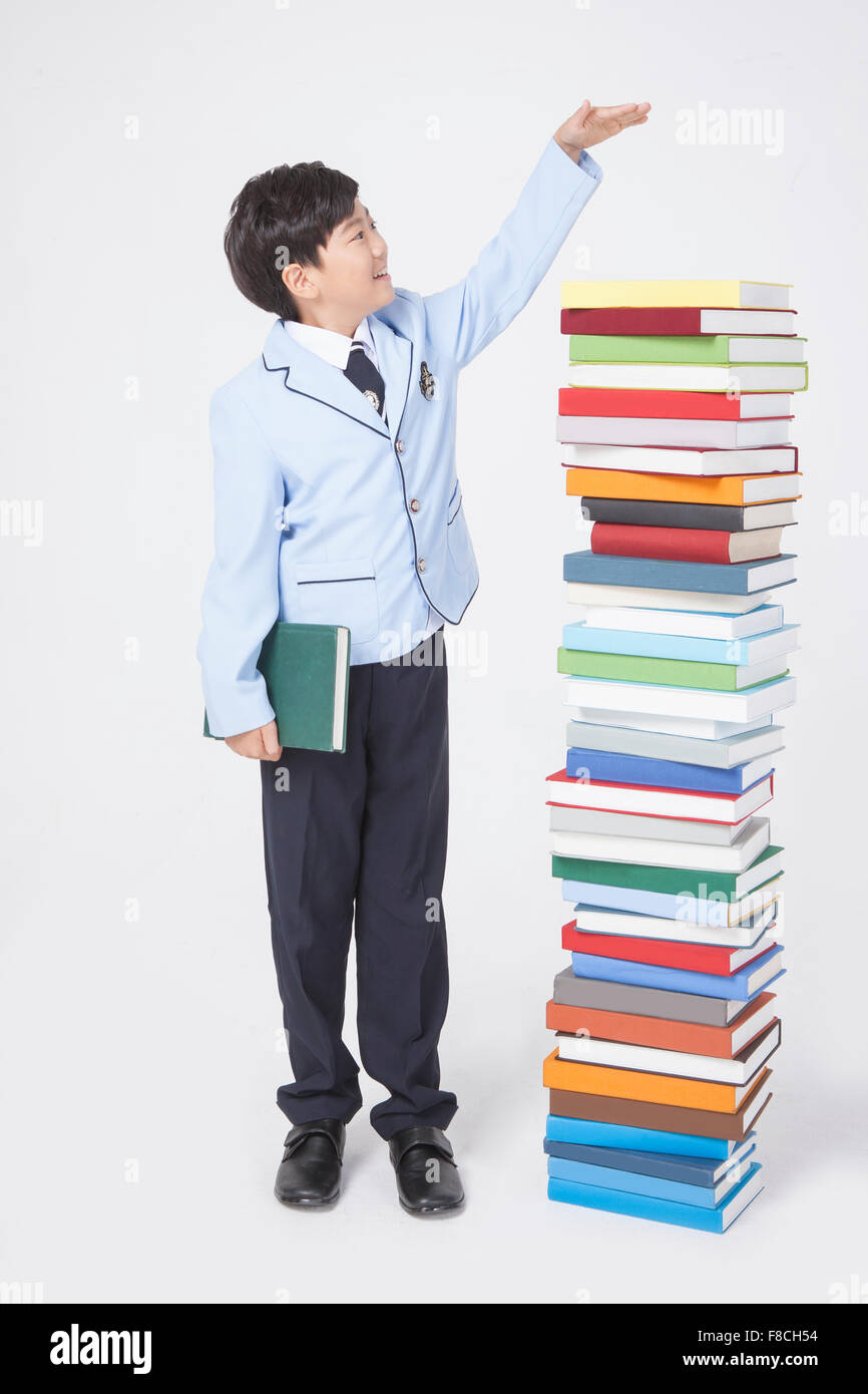 Elementary school boy in school uniforms holding a book and gesturing measuring the height of a pile of books Stock Photo