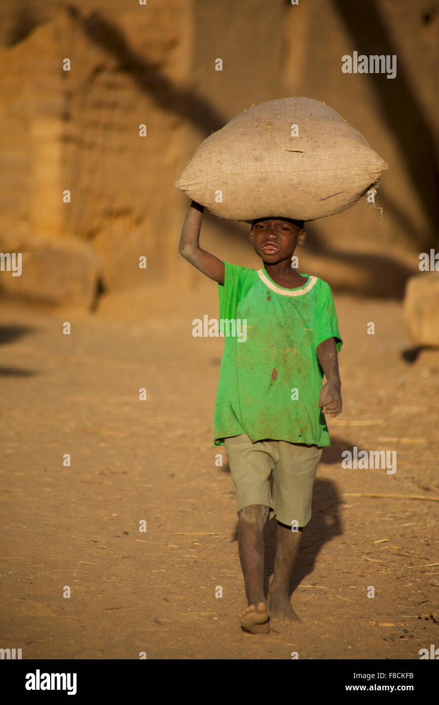 Boy carrying a bag of rice in the Dogon Land in Mali Stock Photo