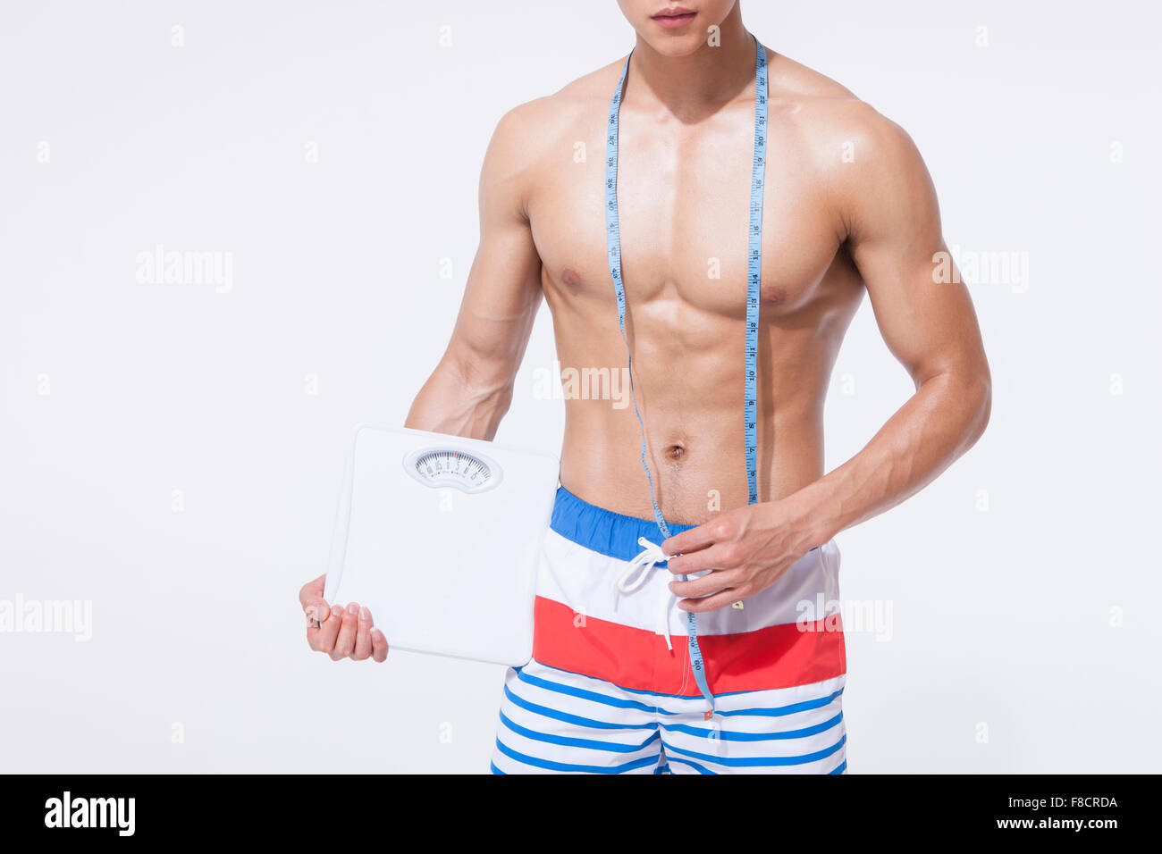 Muscular body of a man with a tapeline around his neck and holding a scale in one hand Stock Photo