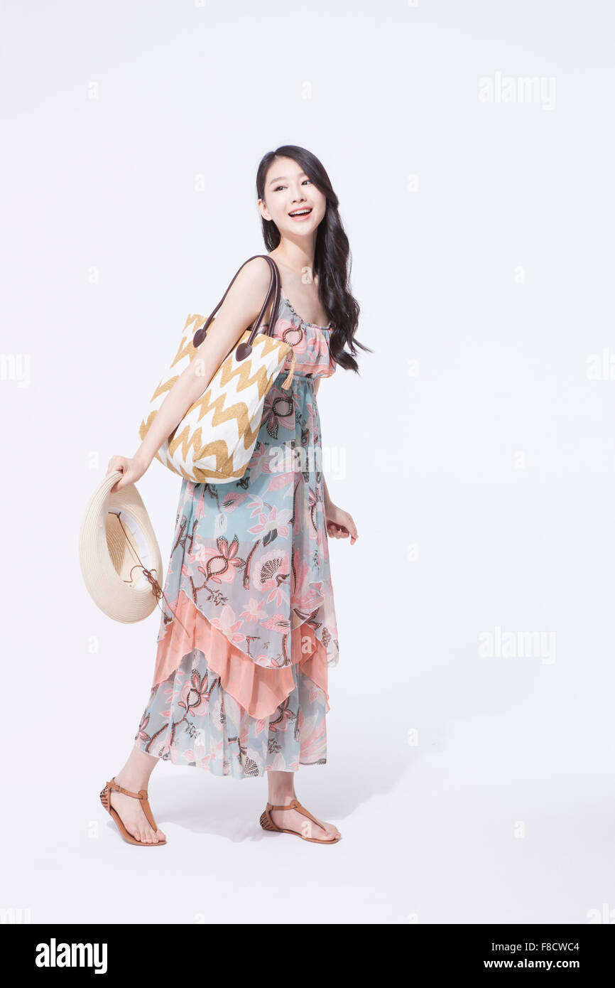 Woman with long hair in maxi dress and sandals standing and holding a hat  with her bag on her shoulder Stock Photo - Alamy