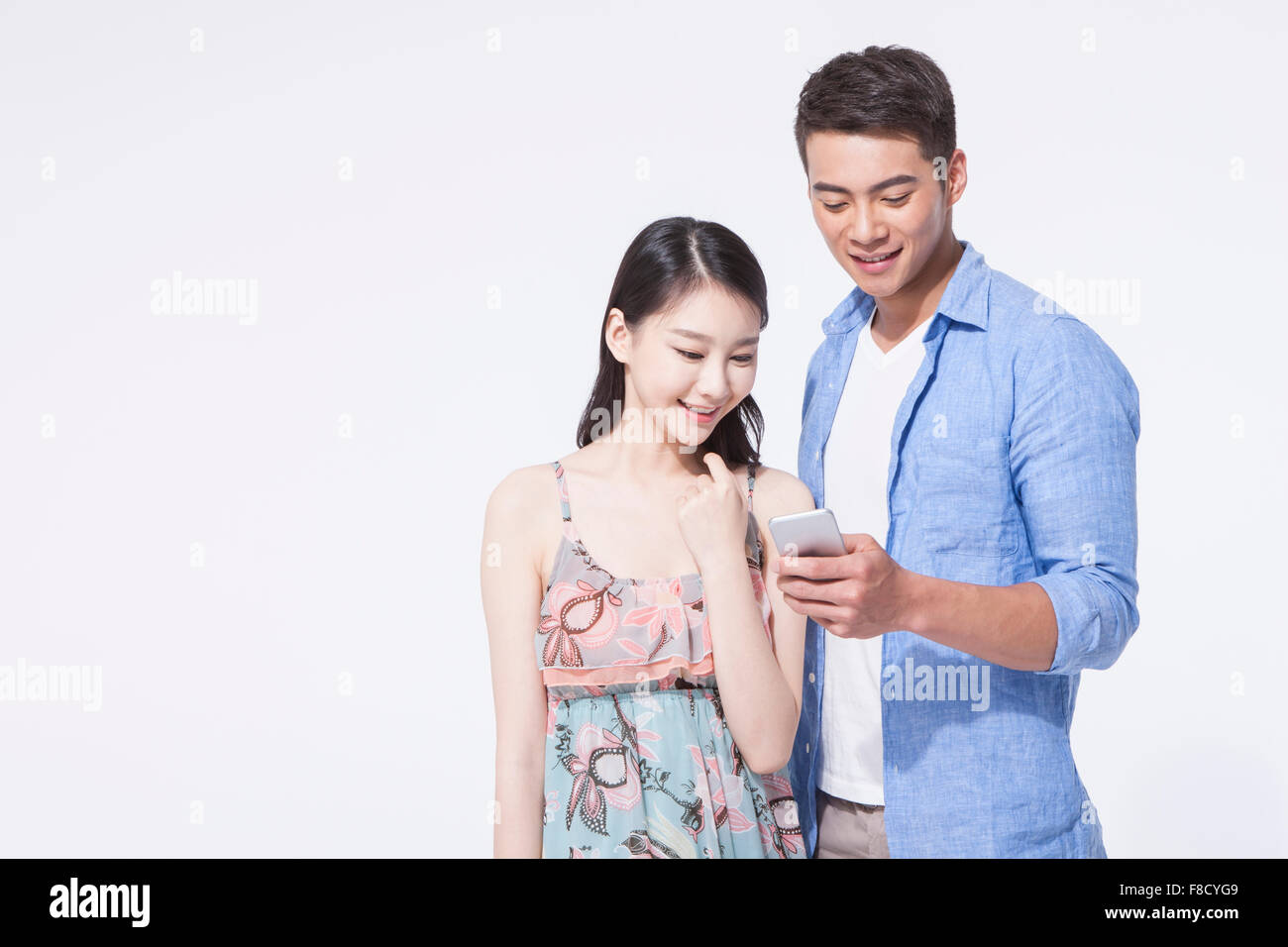 Woman in dress and man in casual outfits looking at man's phone together with a smile Stock Photo