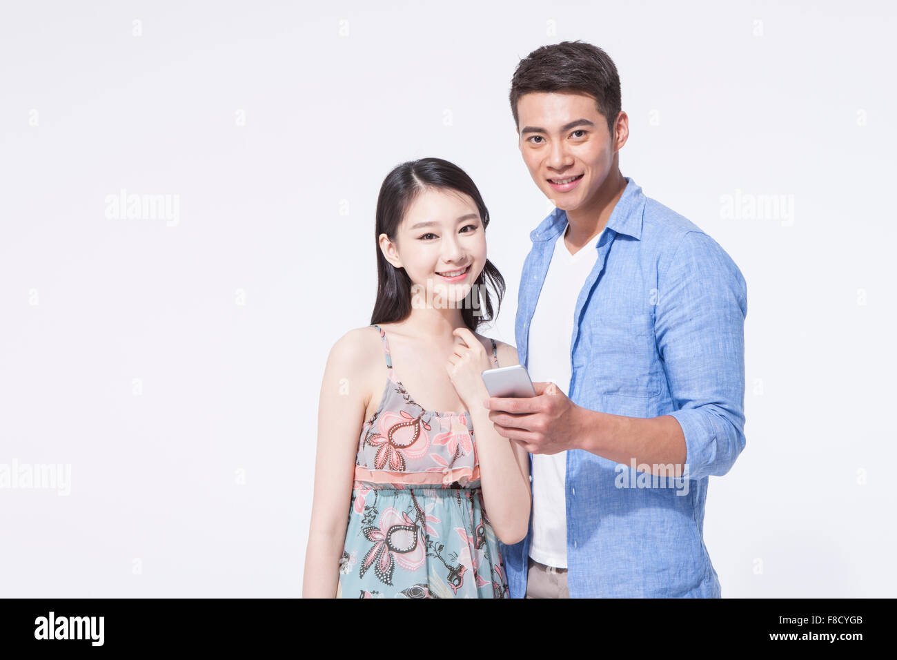 Woman in dress and man in casual outfits together and man holding his phone both staring forward with a smile Stock Photo