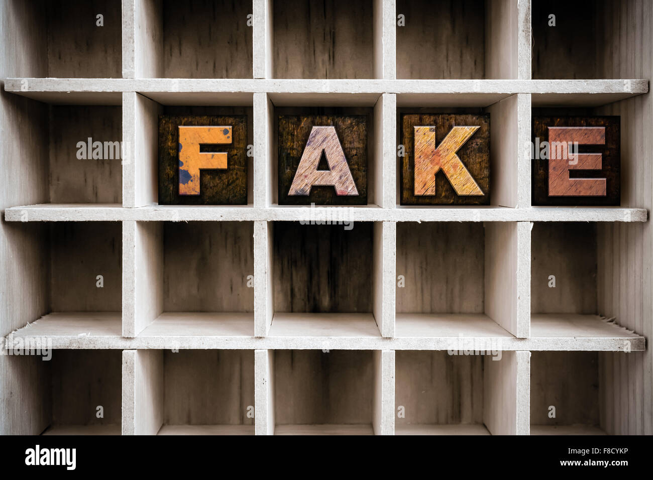 The word "FAKE" written in vintage ink stained wooden letterpress type in a partitioned printer's drawer. Stock Photo