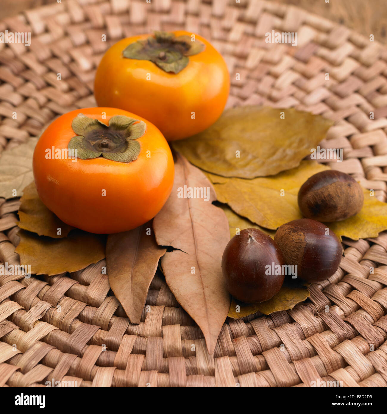 Two persimmons and three chestnuts on fallen leaves Stock Photo