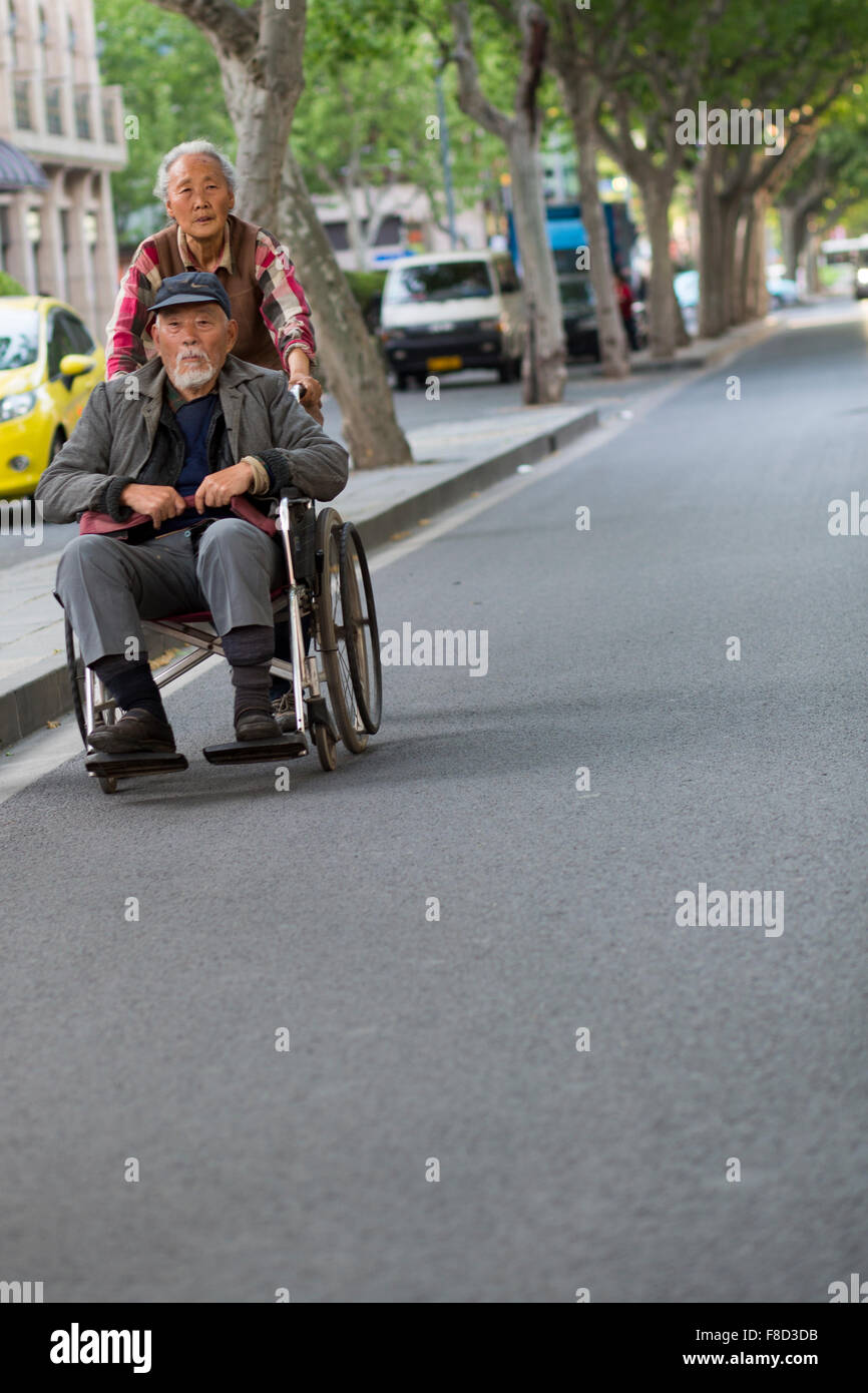 Woman pushing an old man in a wheelchair in the street of Shanghai Stock Photo