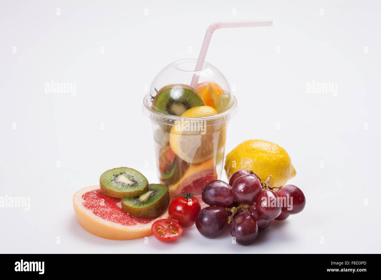 Plastic cup filled with fresh slices of fruits with straw surrounded by variety of fruits Stock