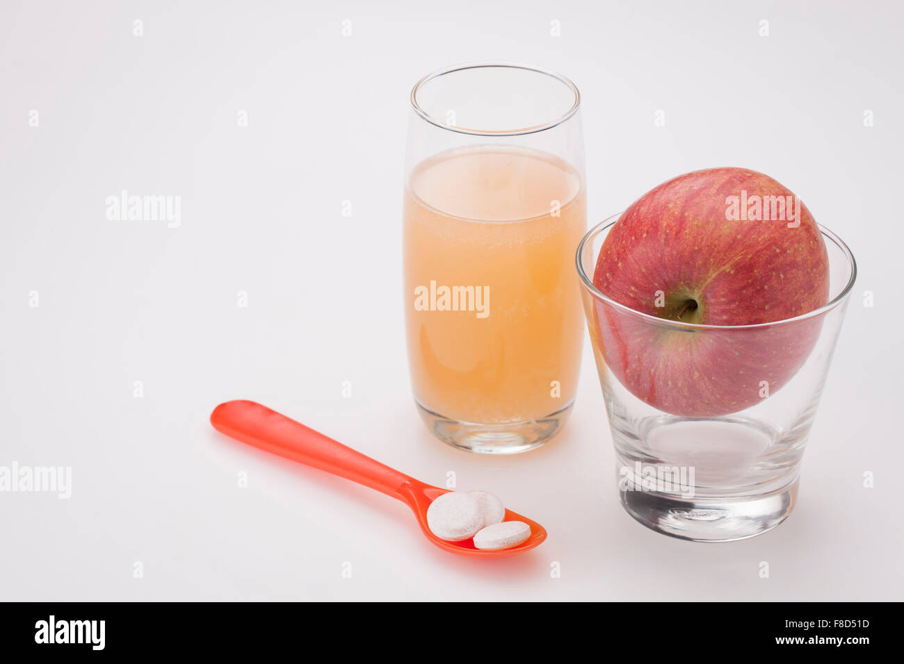 Spoon of vitamin pills and a glass of apple juice with an apple in another empty glass Stock Photo