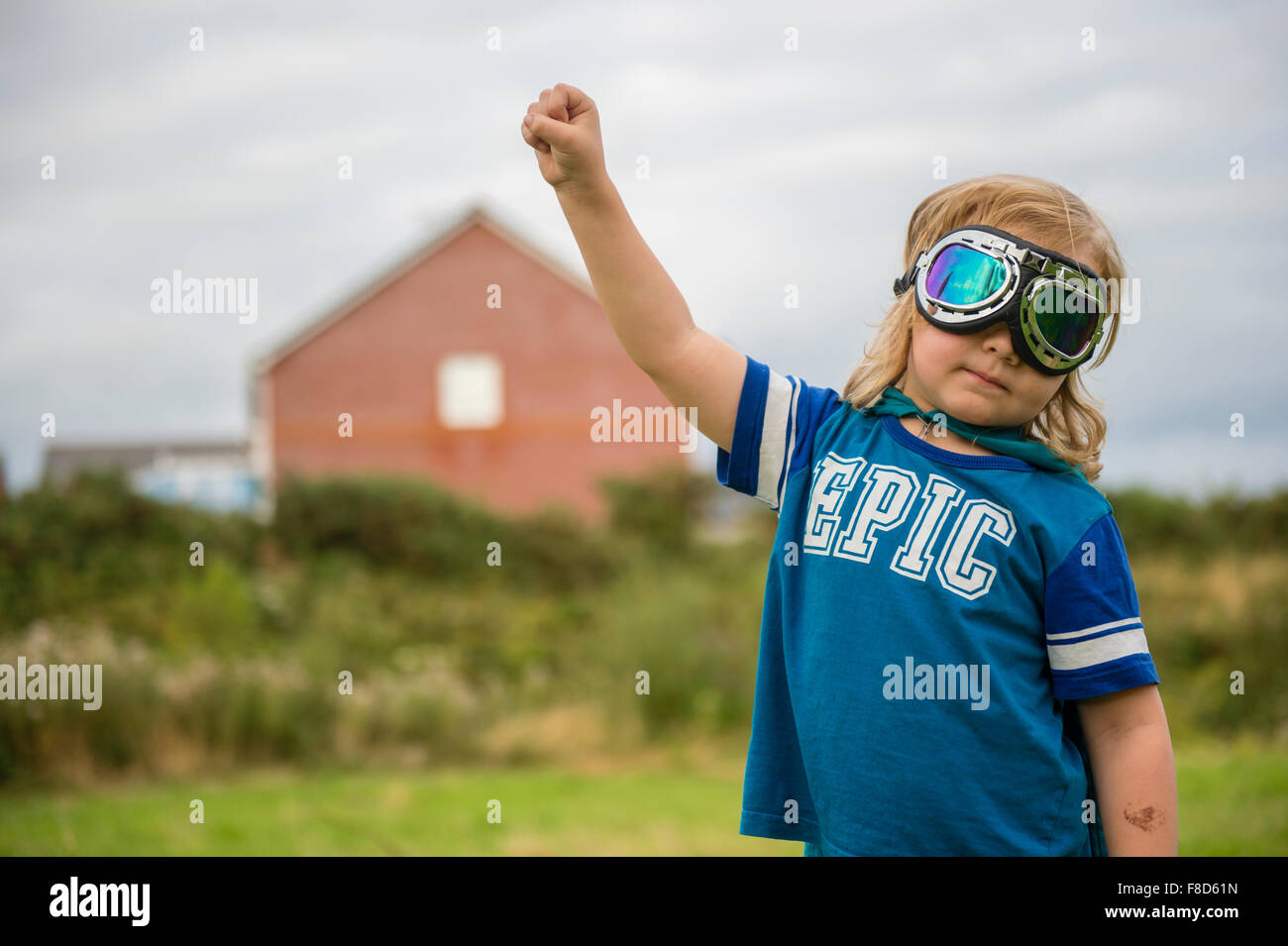 A small pre-teen boy in a home made costume and goggles  dressed up and playing outdoors at being Mini Superhero  on a summer evening , UK Stock Photo