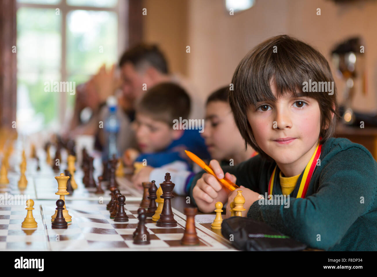Serious little boy playing chess with other students Stock Photo