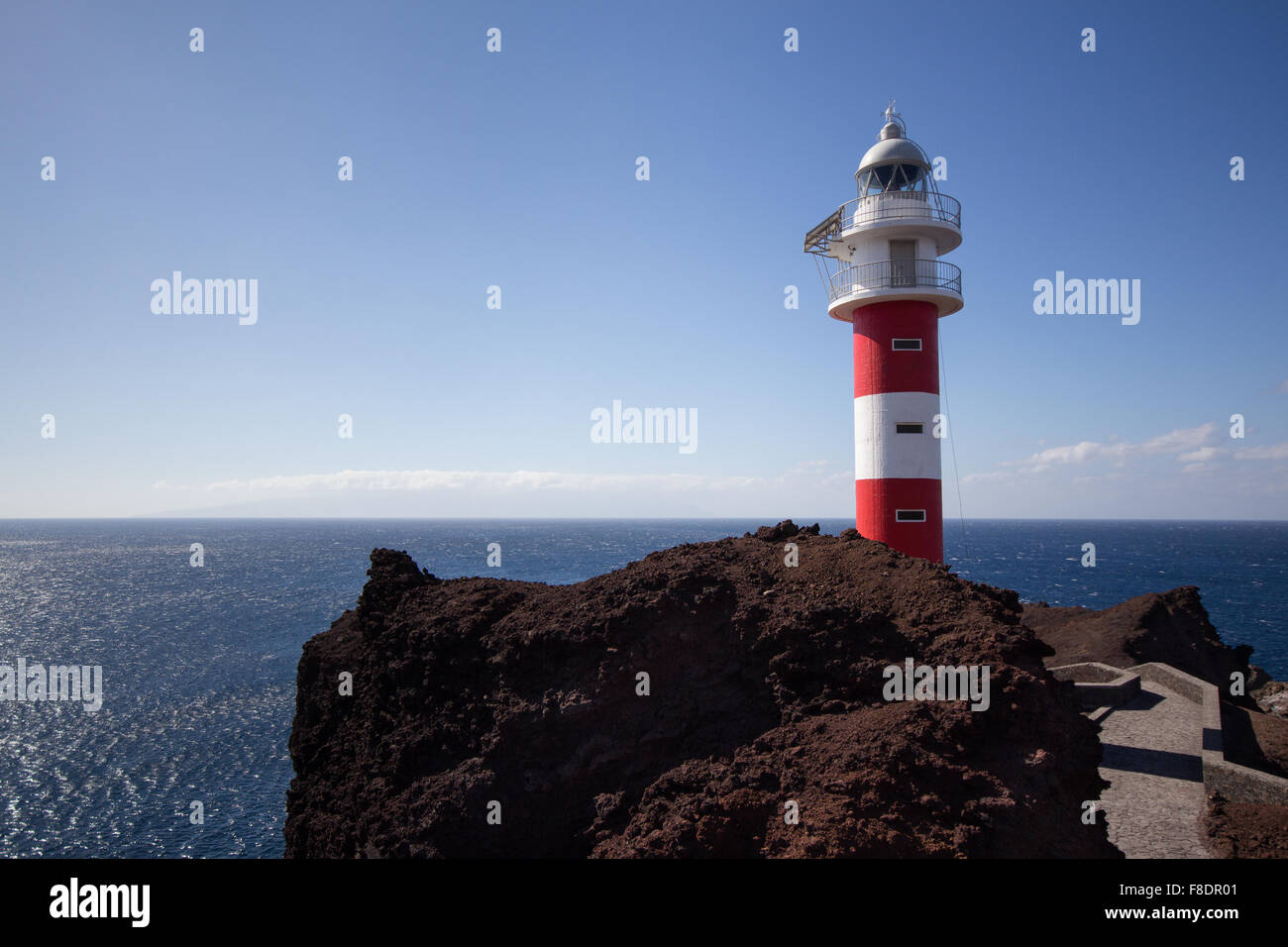 red, white lighthouse with ocean background on rock Stock Photo