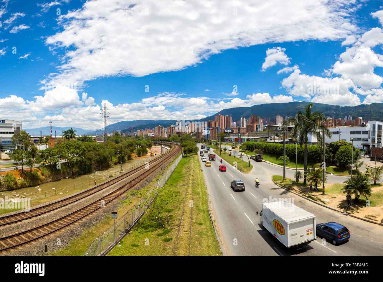 Outdoors view of the Medellin metro line with train, railway tracks, river and cityscape with traffic on the road. Colombia 2015 Stock Photo