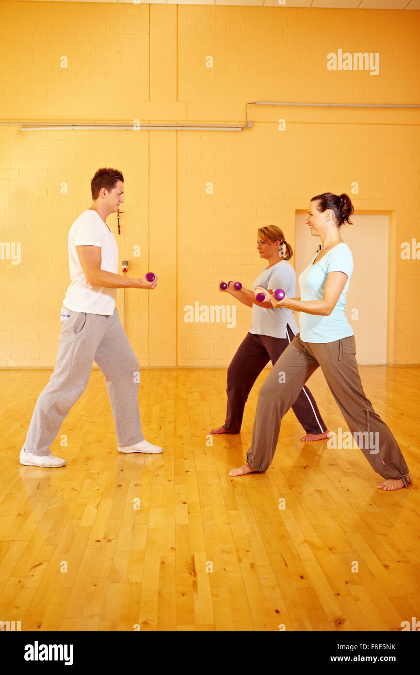 Two women doing dumbbell exercises with personal trainer in gym Stock Photo