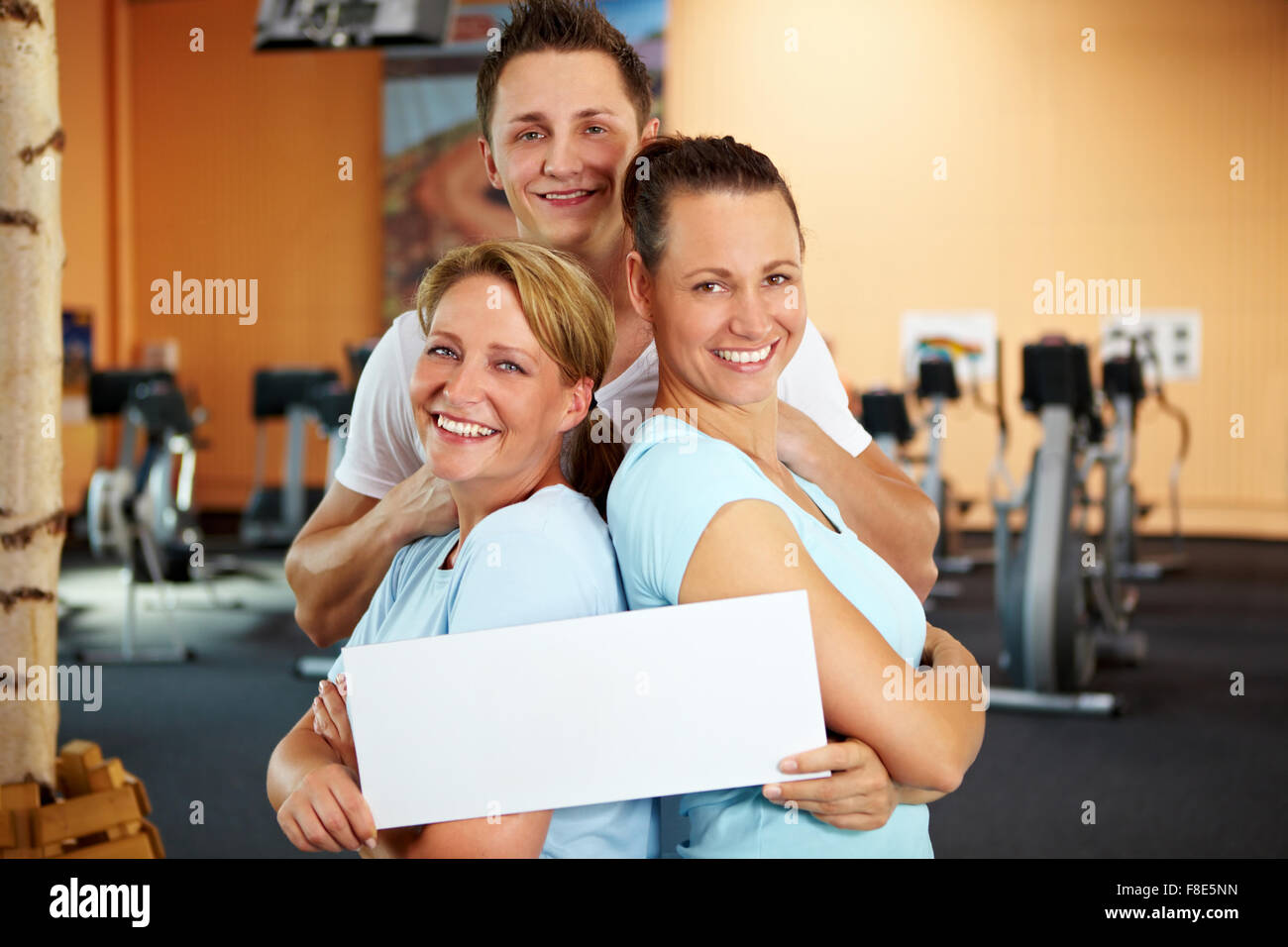 Two women and a man holding an empty sign in a gym Stock Photo