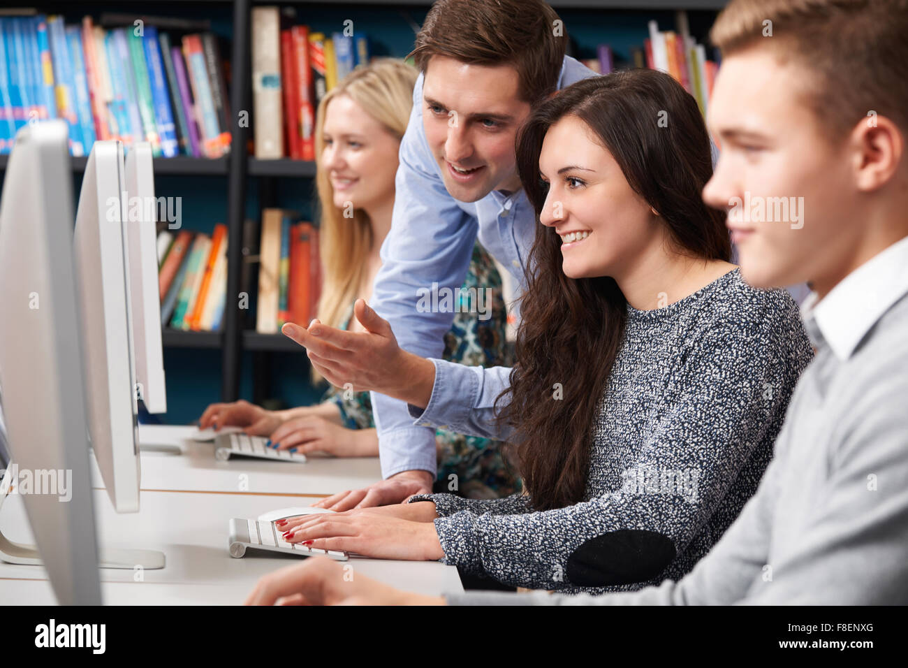 Tutor Helping Teenage Students Working At Computers Stock Photo - Alamy