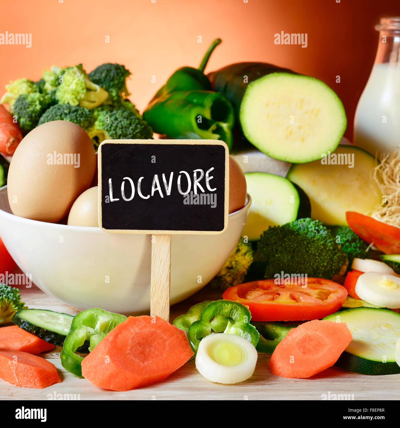 closeup of a signboard with the word locavore on a table full of different raw vegetables, a bowl with some chicken eggs and a b Stock Photo