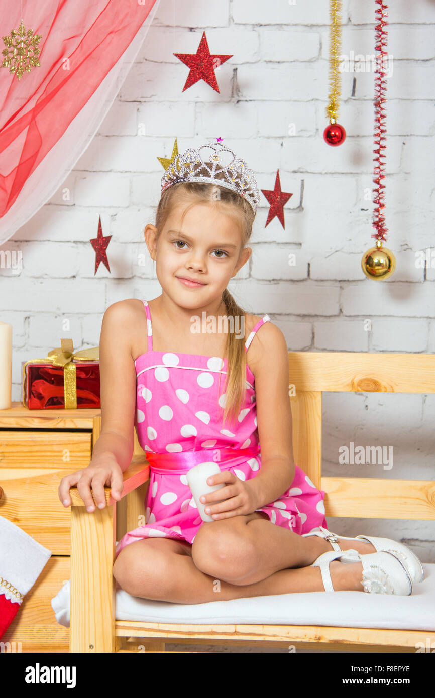 Six year old girl sitting on a bench with a small gift from snowy Christmas trees Stock Photo