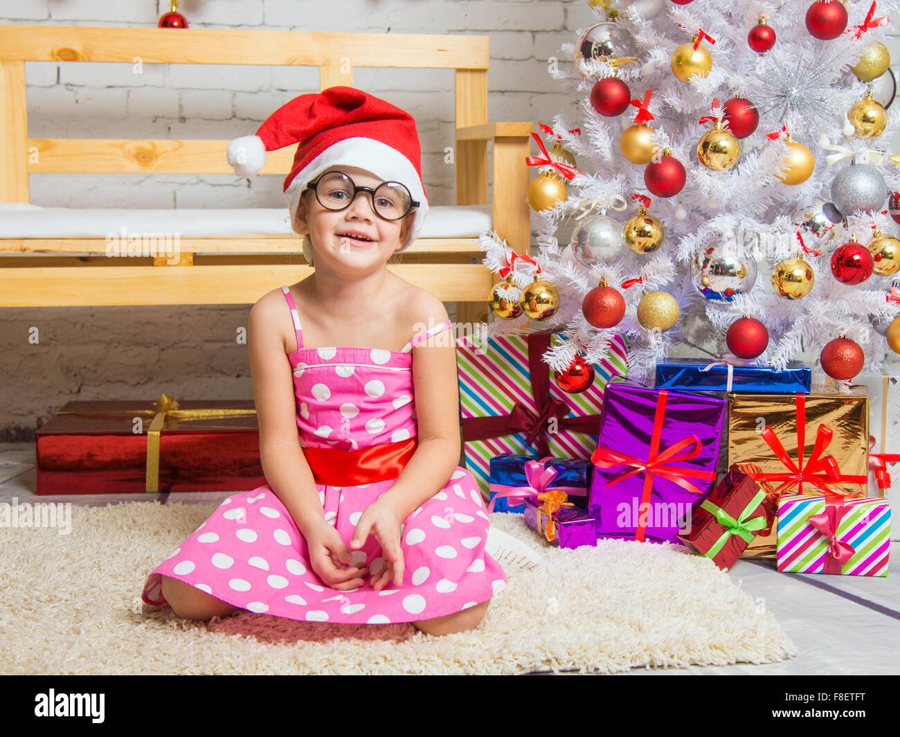 Girl in the red hat and the funny round glasses sits on a rug in the room with New Years interior Stock Photo
