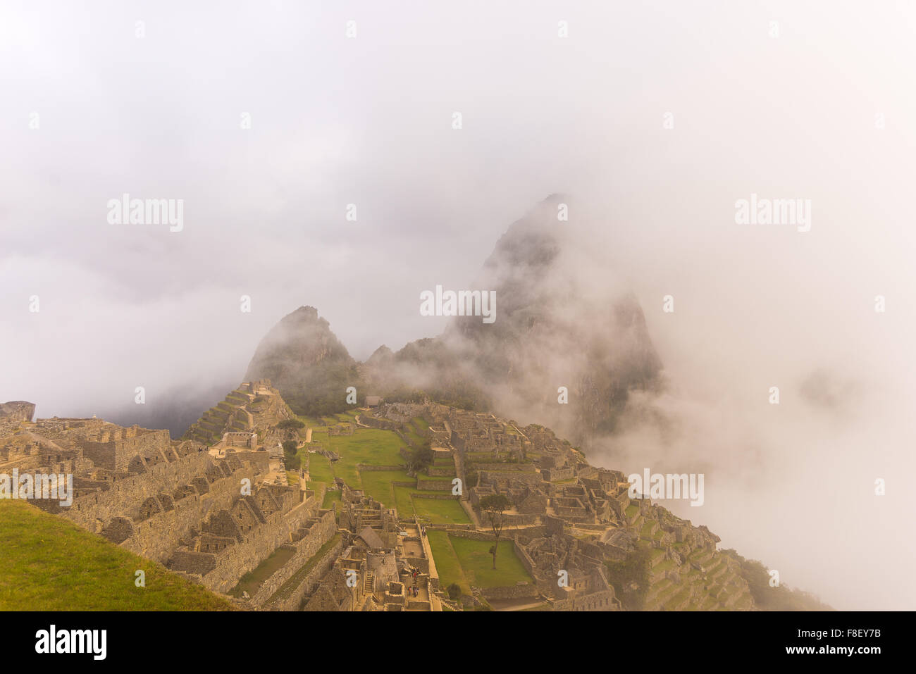 Machu Picchu illuminated by the first soft sunlight coming out from the opening clouds. Mist, clouds and fog composing an idylli Stock Photo