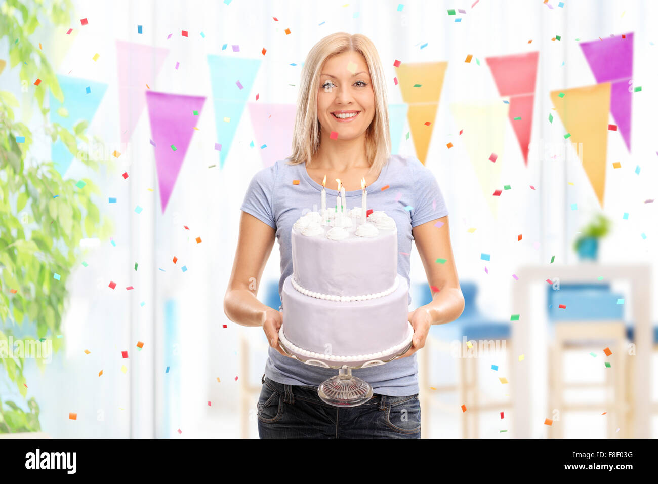 Cheerful young woman holding a birthday cake and looking at the camera at homed Stock Photo