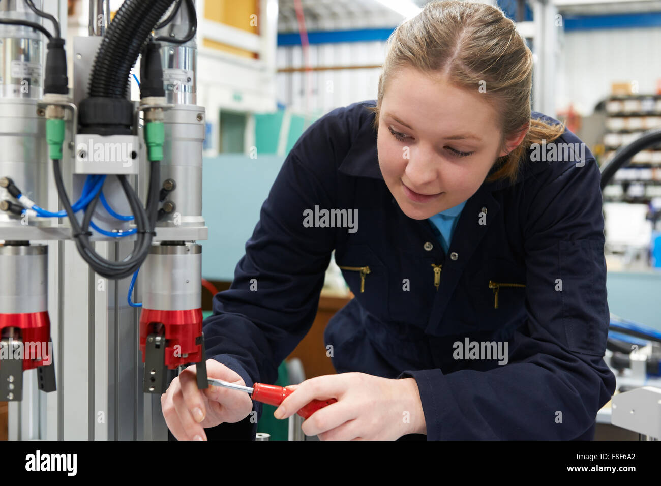 Female Apprentice Engineer Working On Machine In Factory Stock Photo