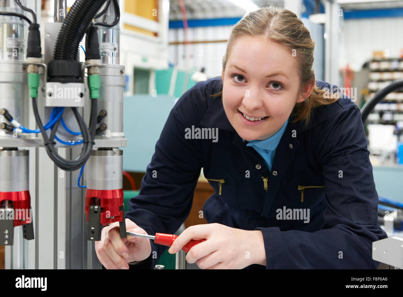 Female Apprentice Engineer Working On Machine In Factory Stock Photo