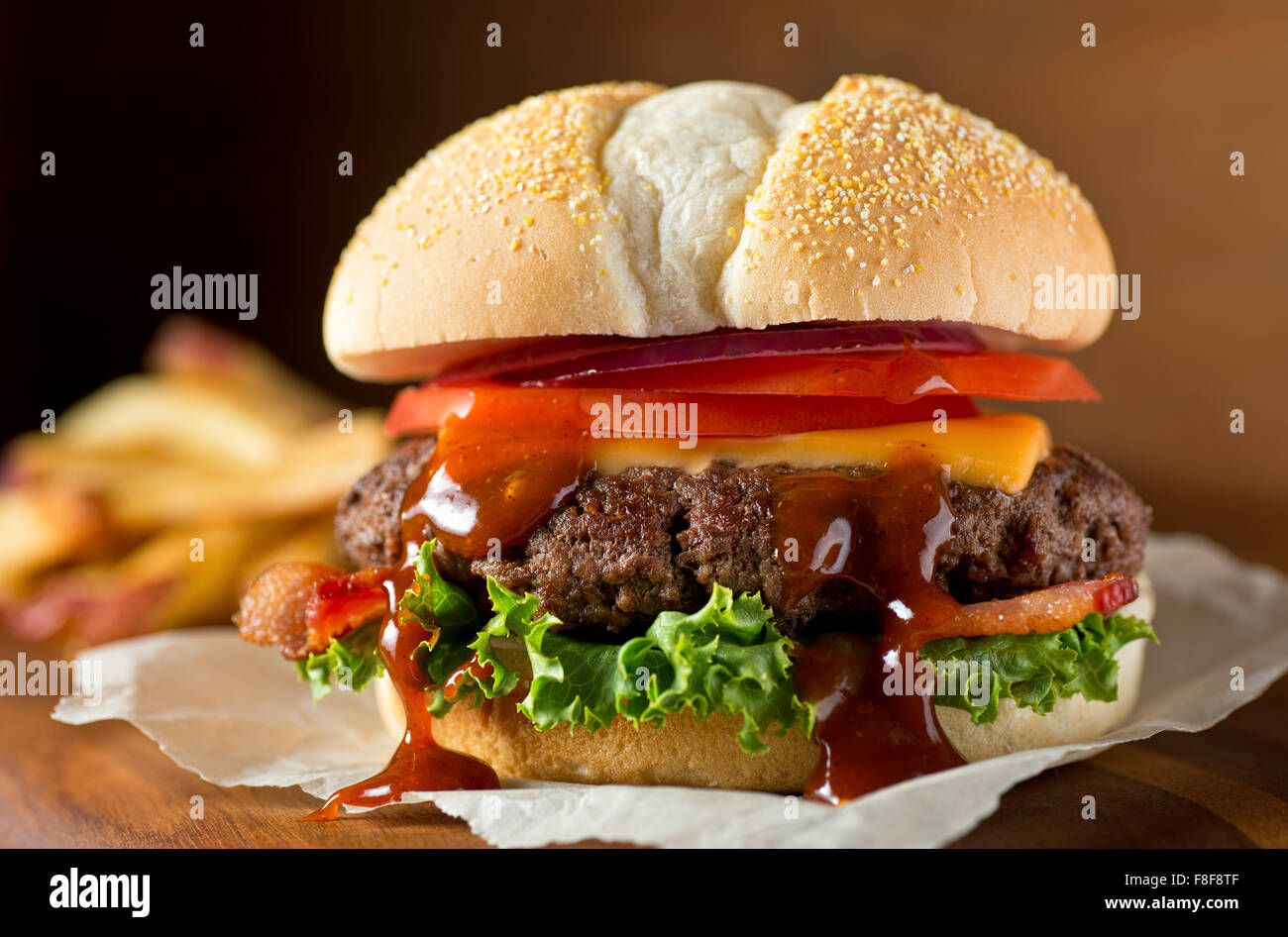 A delicious messy homemade bacon cheeseburger with barbecue sauce, lettuce, tomato, and onion. Stock Photo